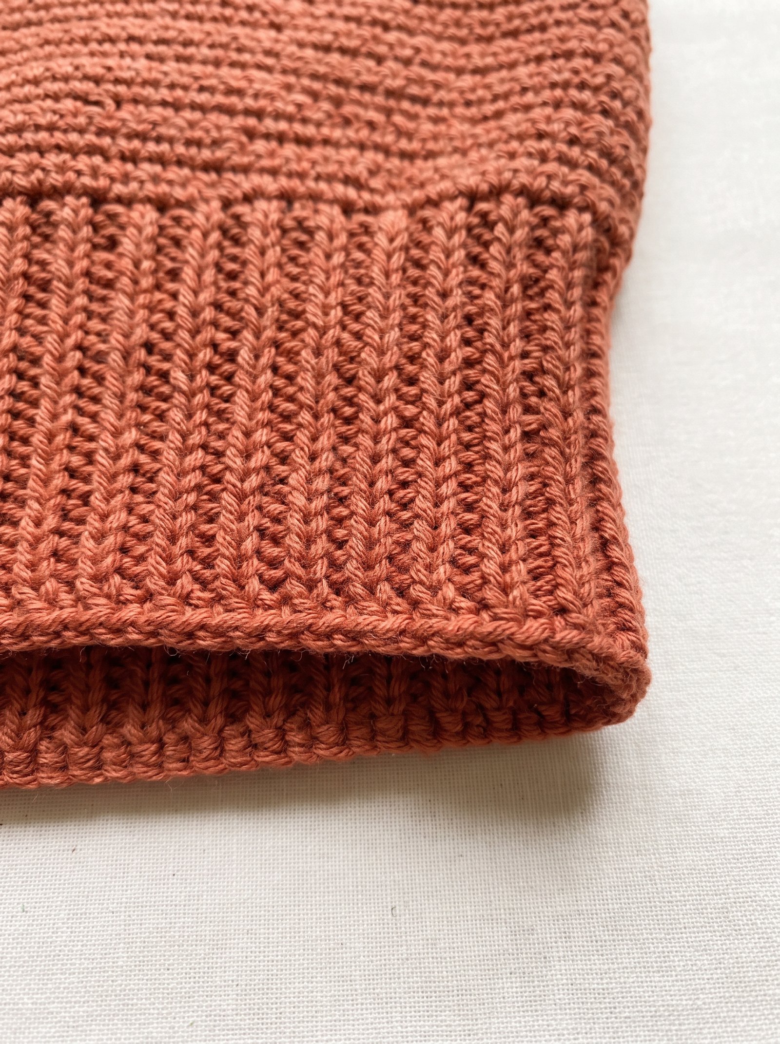 A terracotta crochet ribbed waistband folded over an oak surface showing precise stitch elasticity