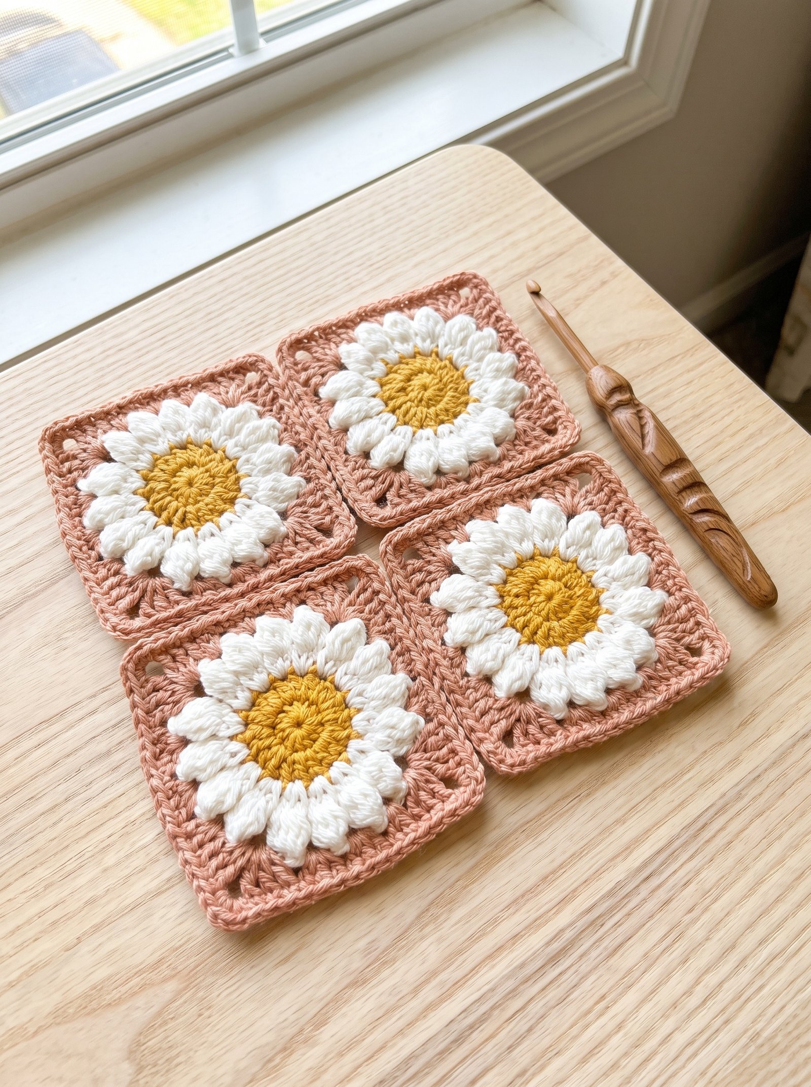 Four crisp crochet daisy granny squares in cream, golden yellow, and olive green resting on an ash wood workbench beside a birch hook and brass snips