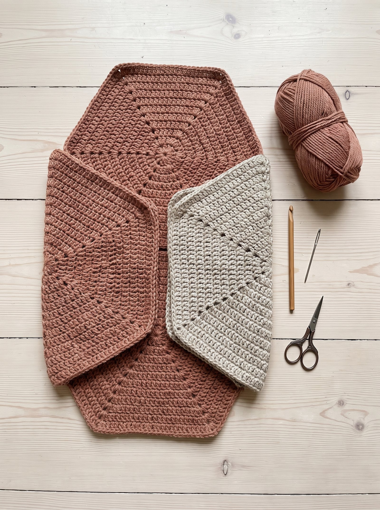 Overhead flat lay of two folded crochet hexagons in muted clay and oatmeal yarn aligned to form a cardigan shrug