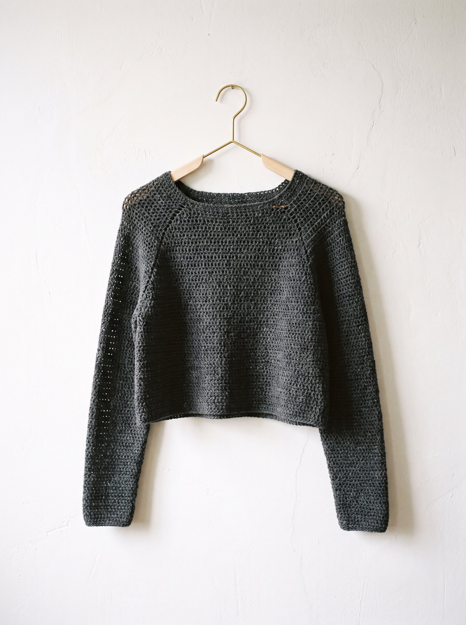 A sleek minimalist charcoal grey crochet shrug with subtle raglan seam shaping on a dress form