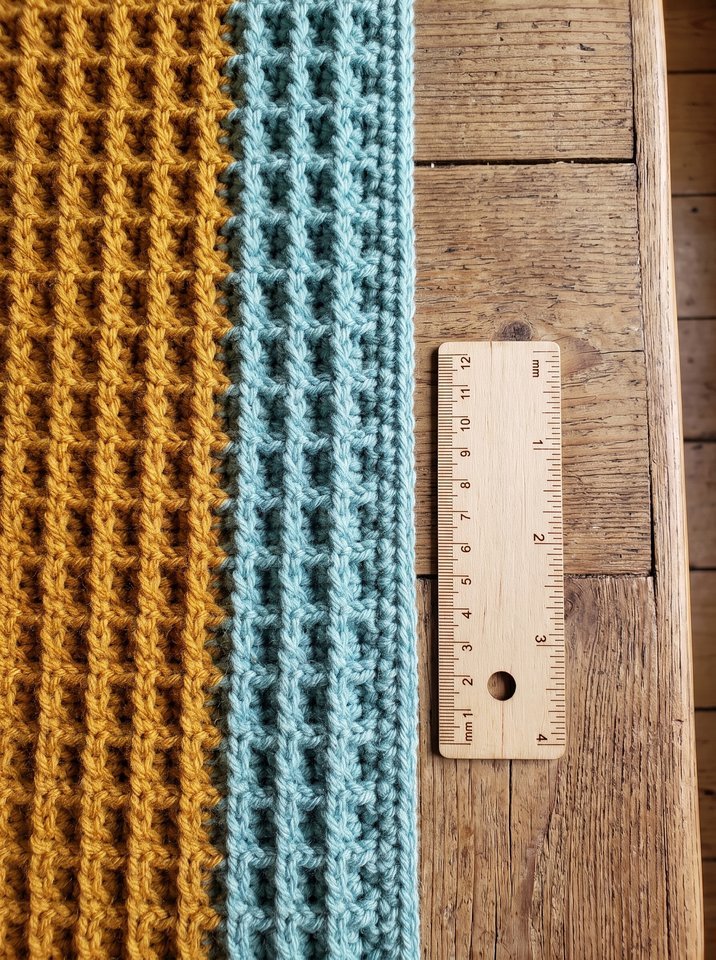 Top-down view of perfectly straight crochet blanket selvage aligned against a wooden ruler