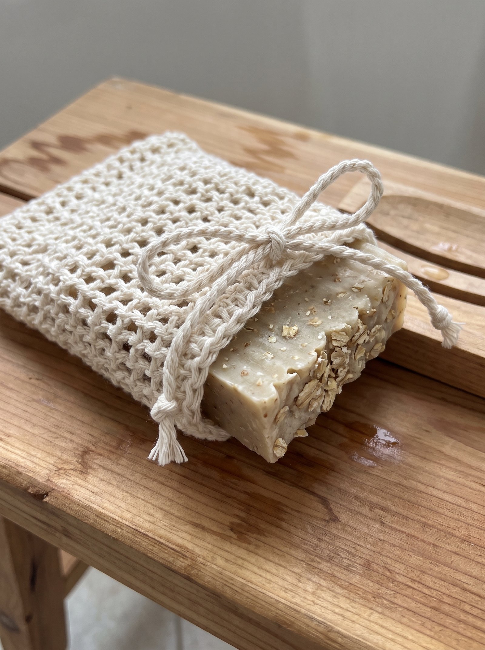 Ecru crochet open mesh soap pouch holding an artisan soap bar beside a cedar bathroom bench