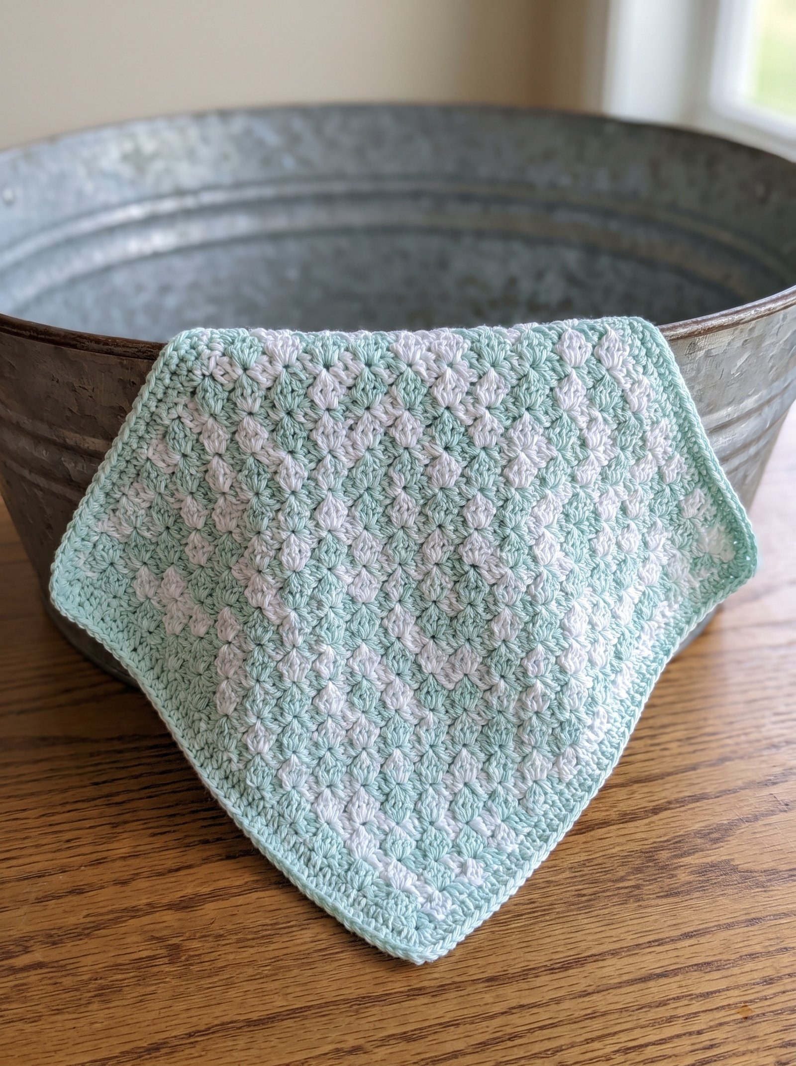 Diagonal pastel mint and white corner-to-corner washcloth draped over a rustic metal basin
