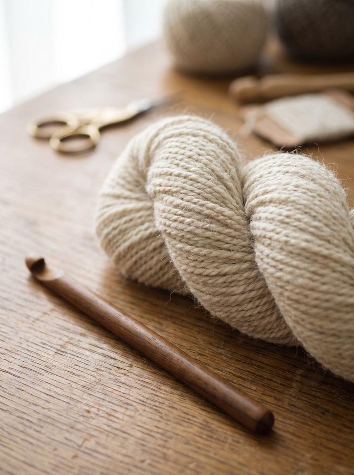 Dark teak crochet hook with oatmeal heather yarn showing foundation chain stitches resting on an oak table