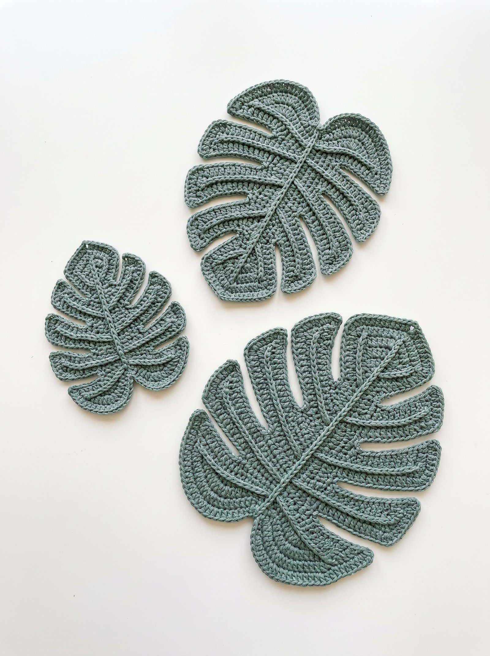 Three graduated crochet monstera leaf trivets in small, medium, and large with raised surface rib veins displayed on a clean white backdrop