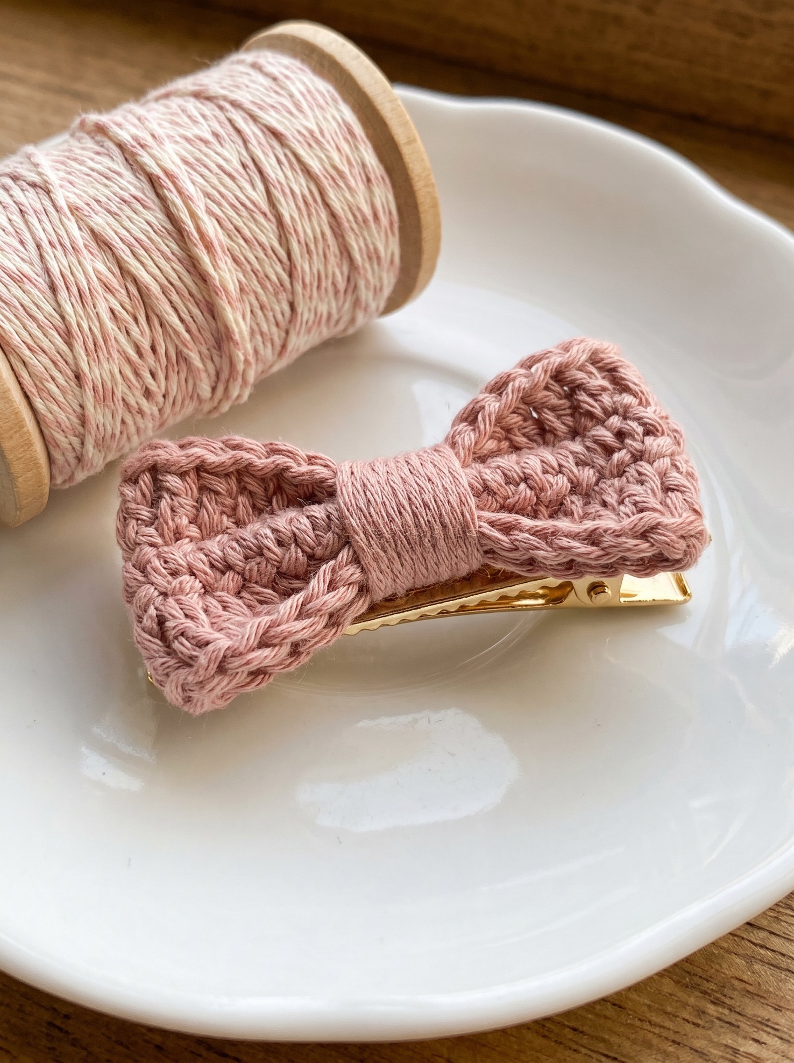 Blush pink crochet mini bow mounted on a gold alligator hair clip beside craft baker twine