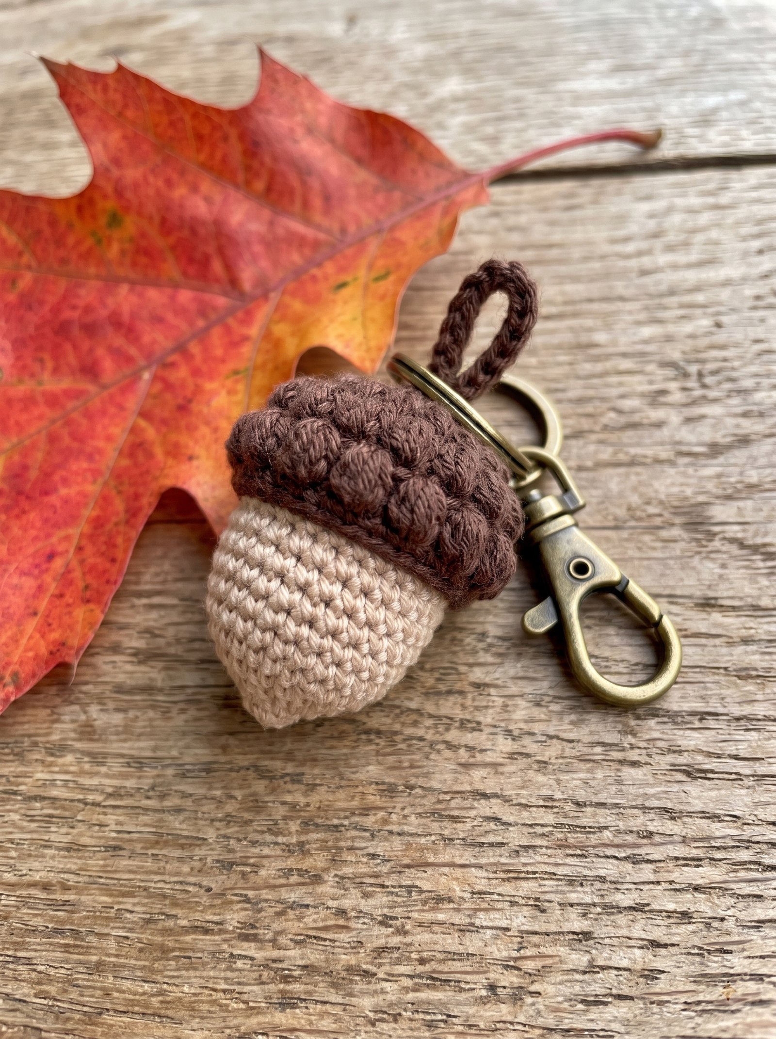 Beige crochet acorn with a textured brown bobble cap attached to a brass keychain clip
