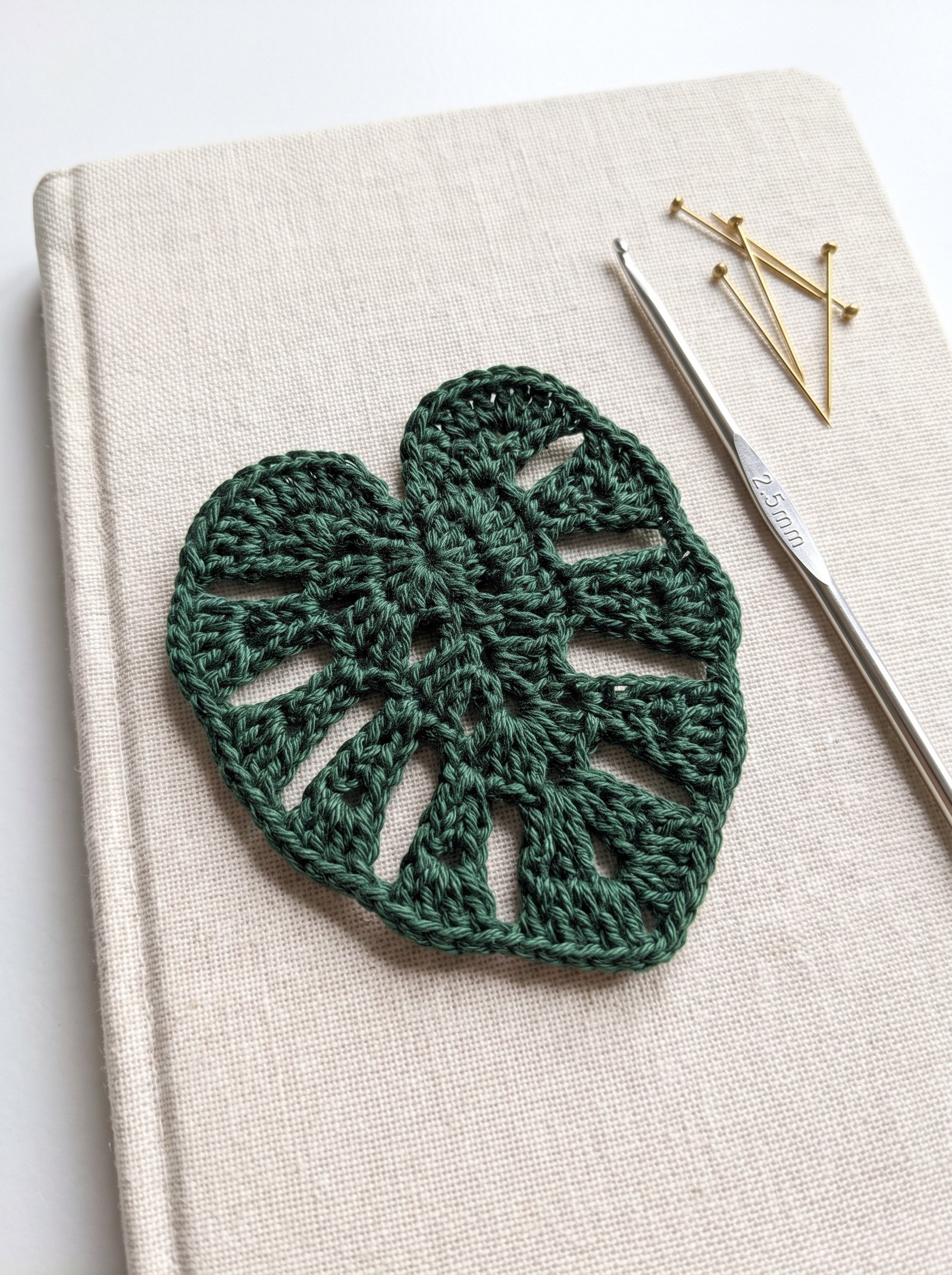 Forest green crochet monstera leaf appliqué on a linen journal cover next to a silver hook