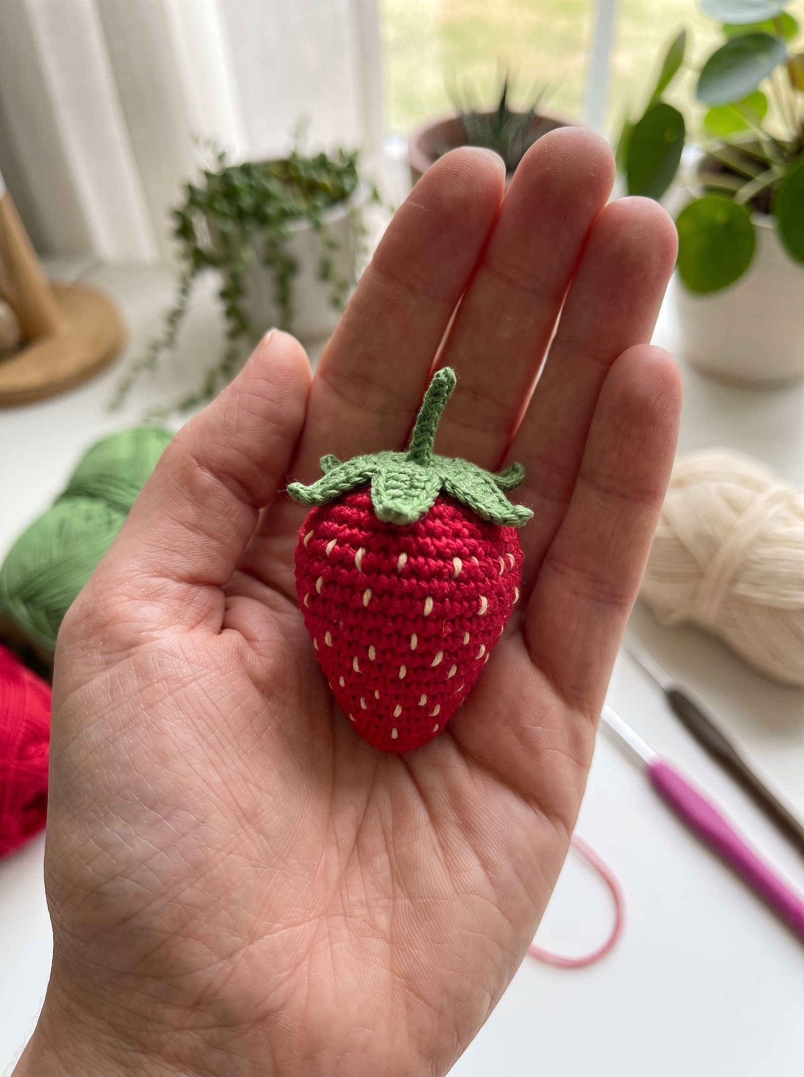 Realistic ruby red crochet amigurumi strawberry with embroidered seeds held in a maker palm